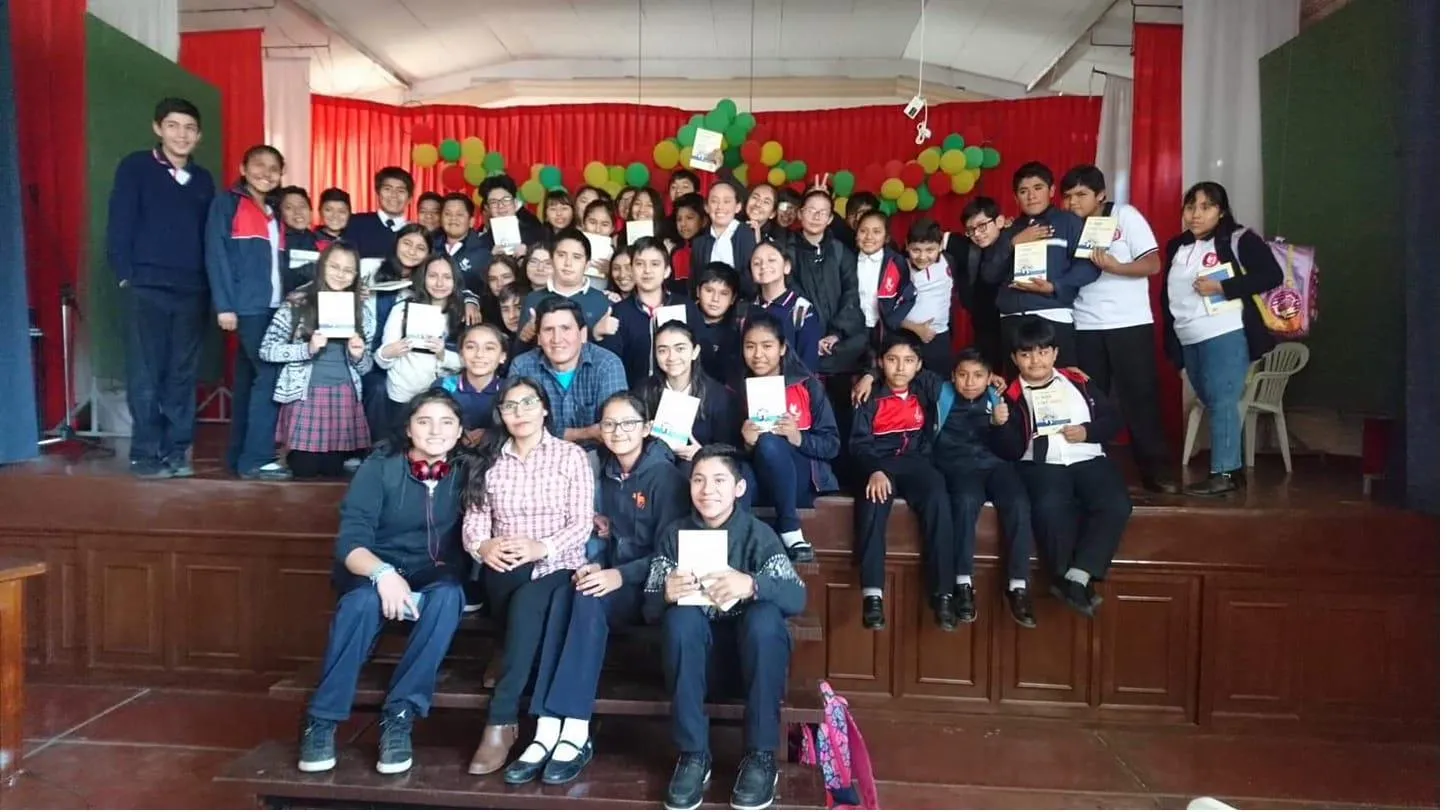 David Vildoso rodeado de niños y niñas con sus libros en un evento escolar